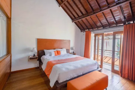 Cozy tropical bedroom with wooden bed, orange accents, and sliding doors to a balcony. - Bali Villas